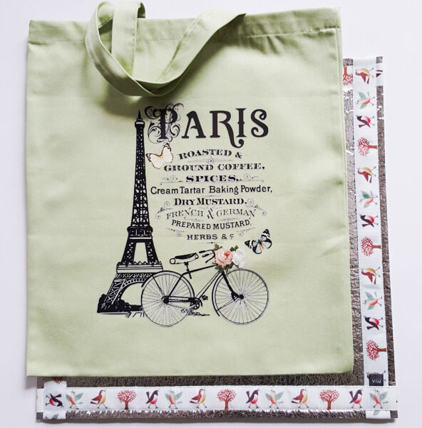 Auf einem Sitzkissen mit dem Motiv "Vogelwelt" liegt eine Stofftasche mit einem Paris-Motiv.